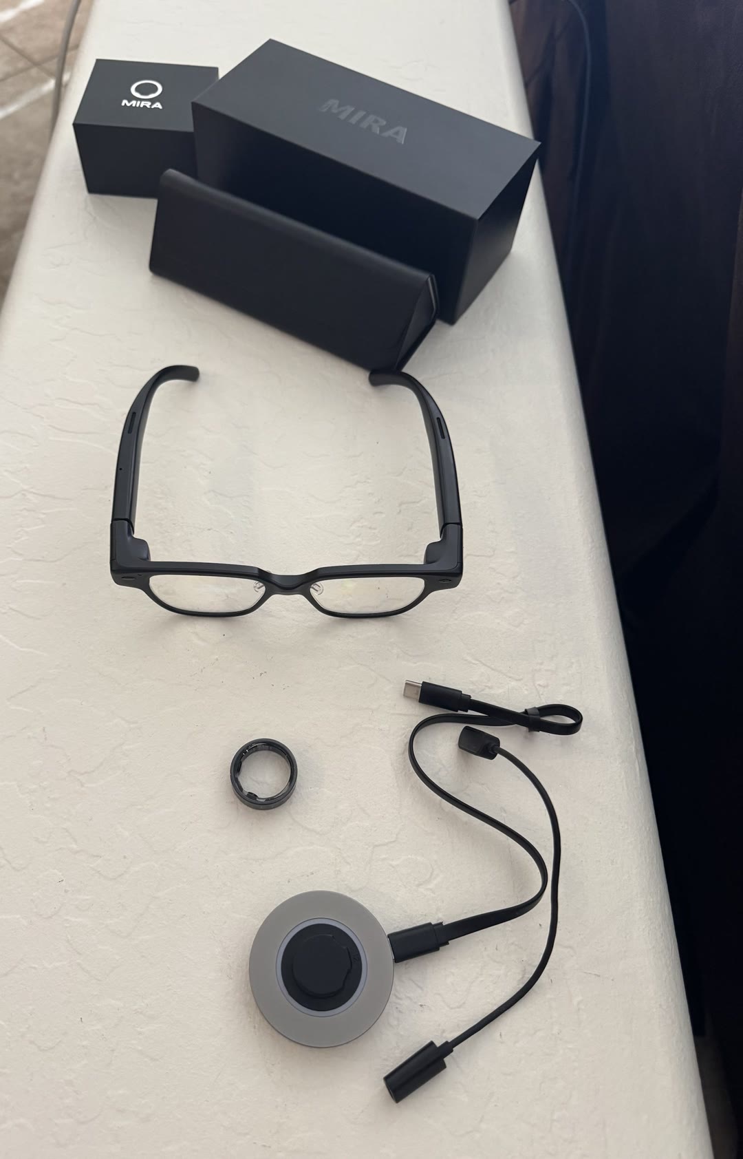 MIRA glasses with the control ring, charging dock, case and boxes laid out on a counter